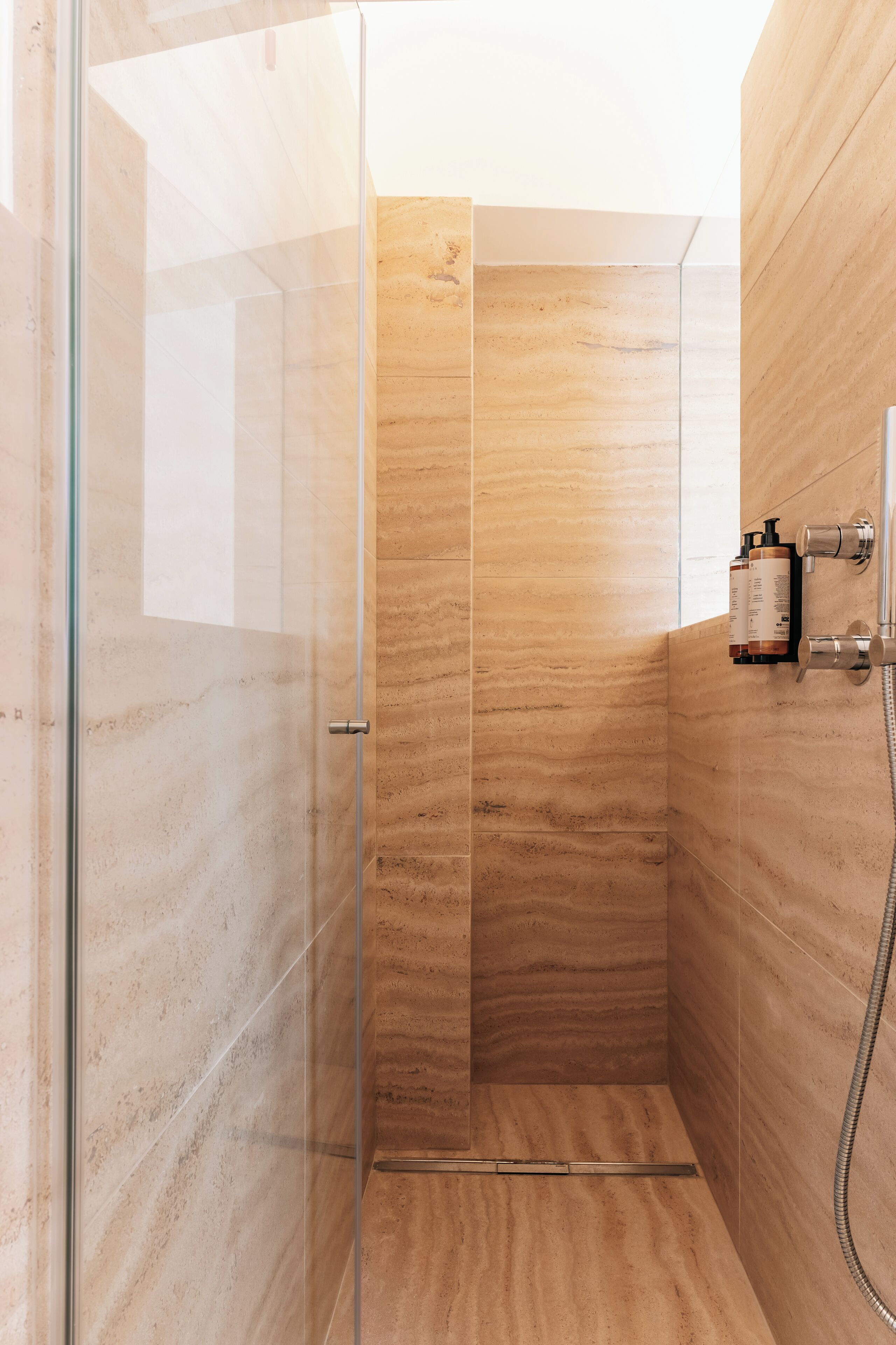 A glass-enclosed shower stall with a marble-like wall and a handheld showerhead.