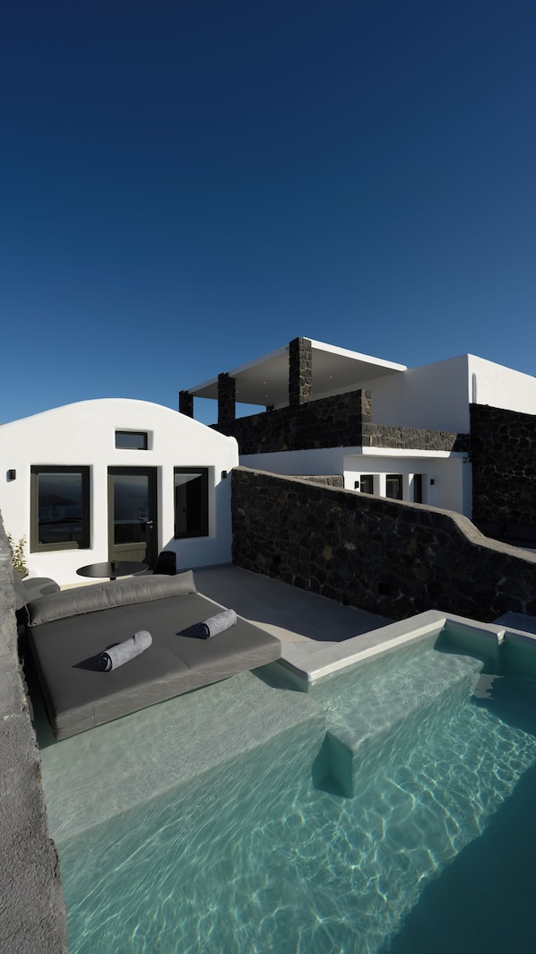 A modern house with a swimming pool, stone walls, and a patio with outdoor furniture. - Arany Terra (Santorini)