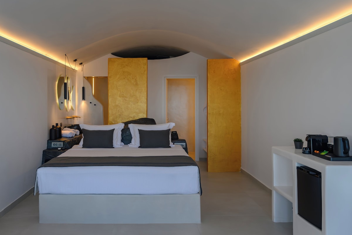 A modern hotel room with a large bed, bedside tables, a coffee machine, and a small plant.