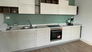 Uma cozinha moderna com armários brancos, forno embutido e parede verde.