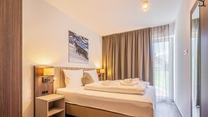 Ein Hotelzimmer mit einem großen Bett, einem Nachttisch, einer Wandlampe und einem Fenster mit Vorhängen.