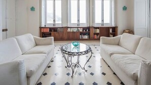 Una sala de estar con dos sofás blancos, una mesa de centro de vidrio y una estantería.