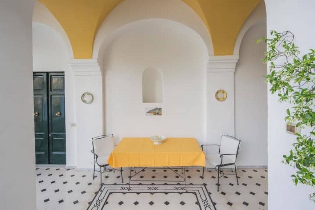 Un coin repas avec une table jaune, deux chaises, un sol à motifs et une porte verte en arrière-plan.
