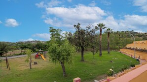 A park with a playground, trees, and a yellow building. - Villaggio La Feluca (Isca sullo Ionio)