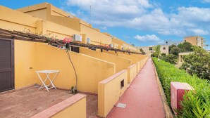 A narrow pathway flanked by yellow buildings with air conditioning units, a red pathway, and greenery. - Villaggio La Feluca (Isca sullo Ionio)