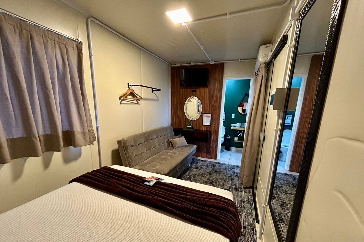 A bedroom with a bed, a sofa, a mirror, and a hanging clothes rack.