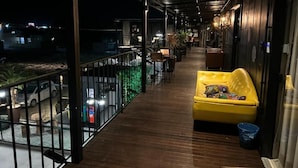 A covered outdoor area with a yellow sofa, wooden flooring, and a railing overlooking a parking area. - Pousada Canto do Gravatá (Penha)