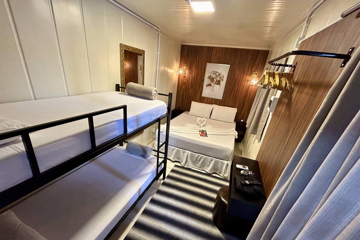 A compact hotel room with bunk beds, a small bedside table, a wall-mounted light fixture, and a framed picture on the wall.