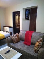 Una sala de estar con un sofá gris, dos cojines estampados, una manta roja y un control remoto sobre una mesita.