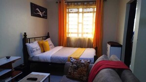 A bedroom with a bed, a sofa, a small table, and a window with curtains.