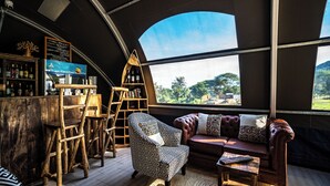Ein gemütliches Interieur mit einer Holztheke, einem gemusterten Sessel und einer Couch mit Kissen.
