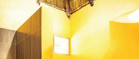 A bathroom with yellow walls, a thatched ceiling, and a tiled floor.