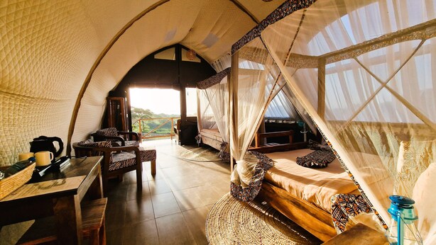 Ein gemütliches, helles Zelt mit Bett, Tisch und Stühlen sowie Blick ins Freie.