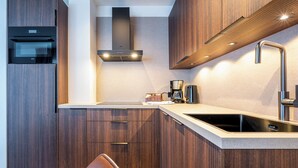 Eine moderne Küche mit Holzschränken, einem eingebauten Ofen, einer Edelstahlspüle und einer Kaffeemaschine.
