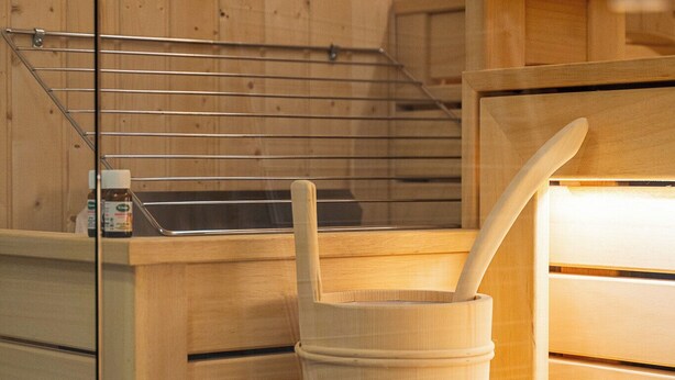Eine Holzsauna mit einer hölzernen Sitzbank, einem Holzfass und einem Metallregal.