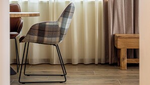 Ein modernes Zimmer mit Holzboden, einem karierten Sessel, einer Holzbank und einem Fenster mit durchsichtigen Vorhängen.