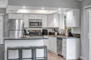 A modern kitchen with stainless steel appliances, white cabinetry, and a central island with bar stools. - Luxury Home w/ Heated Pool & Golf Access (Scottsdale)