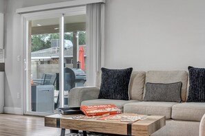 Een woonkamer met een bank, een bijzettafeltje met gezelschapsspellen en een schuifdeur naar buiten.