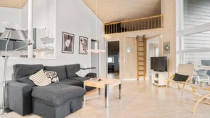 Una sala de estar moderna con un sofá gris, una mesa de centro de madera y un mueble para televisión. Se ve una escalera que conduce a un nivel superior.