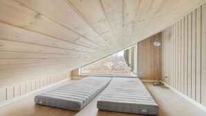 Una habitación con techo inclinado, paredes de madera y un ventanal grande. Hay dos colchones en el suelo.