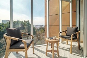 A balcony with two wooden chairs and a small table, overlooking a cityscape.