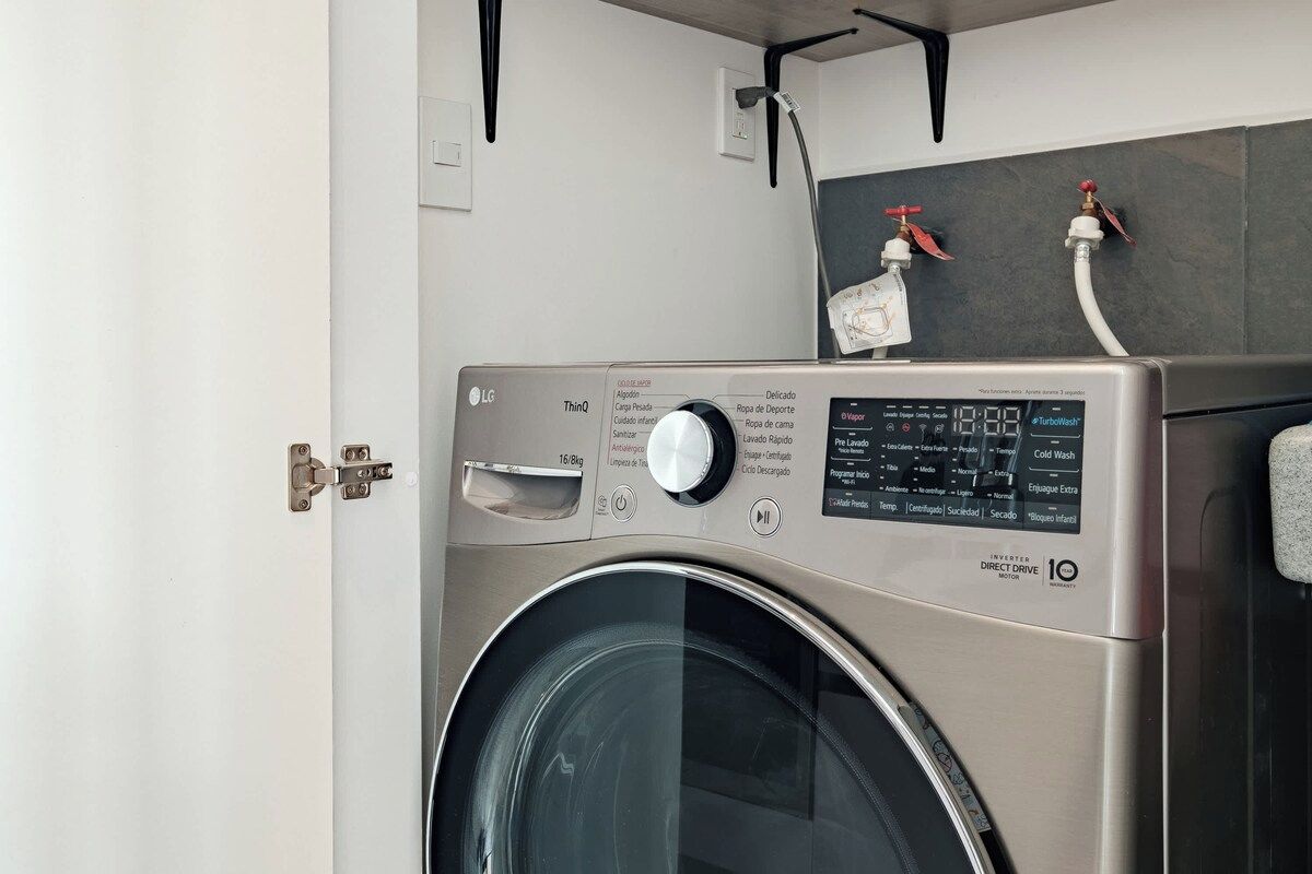 A front-loading LG ThinQ washer with a control panel, a door, and a wall-mounted faucet above it.