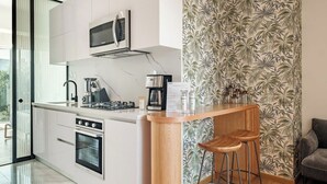 Una cocina moderna con microondas, estufa y cafetera. Cuenta con una barra y taburetes, además de un papel tapiz estampado.