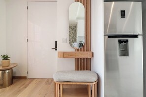 A modern kitchen with a stainless steel refrigerator, a wooden cabinet with a mirror, and a bench.