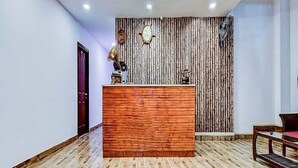 A reception area with a wooden reception desk, a clock on the wall, and a patterned wall in the background. - AVVA Hotels (Kochi)