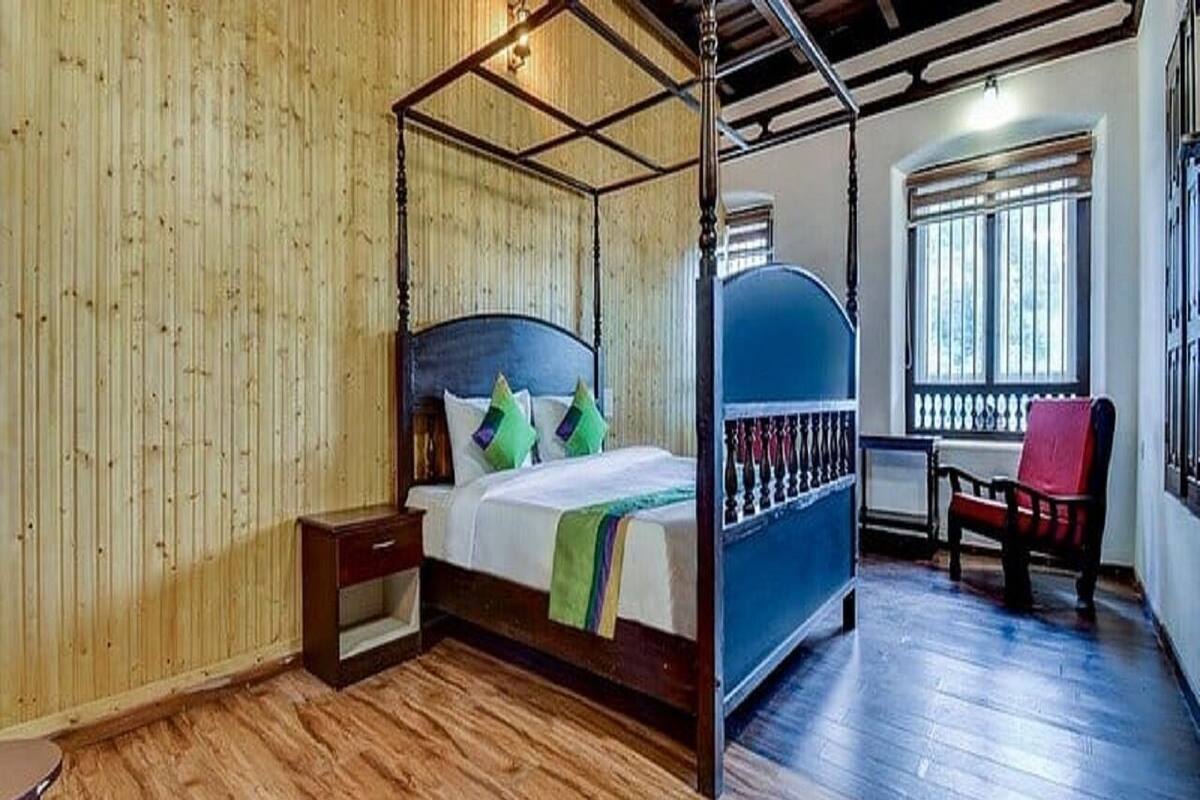 A four-poster bed with a wooden headboard, a nightstand, and a chair by the window.