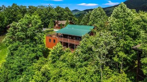 A lodge with a green roof, surrounded by dense forest and mountains.