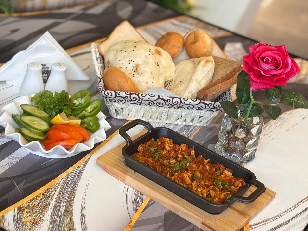 A table with a variety of food items including bread, vegetables, and a dish in a cast iron skillet.