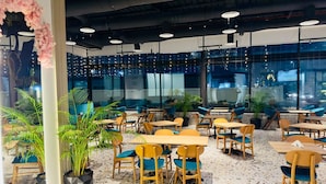 Comedor interior con mesas y sillas, ventanas amplias y plantas en macetas.