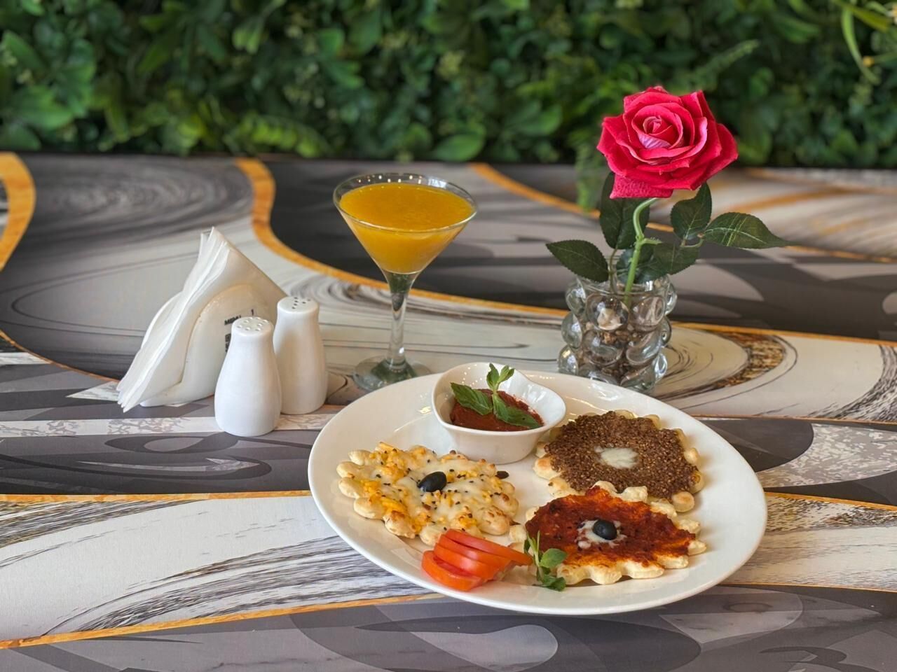 A table with a plate of food, a glass of orange juice, a rose, and salt and pepper shakers.