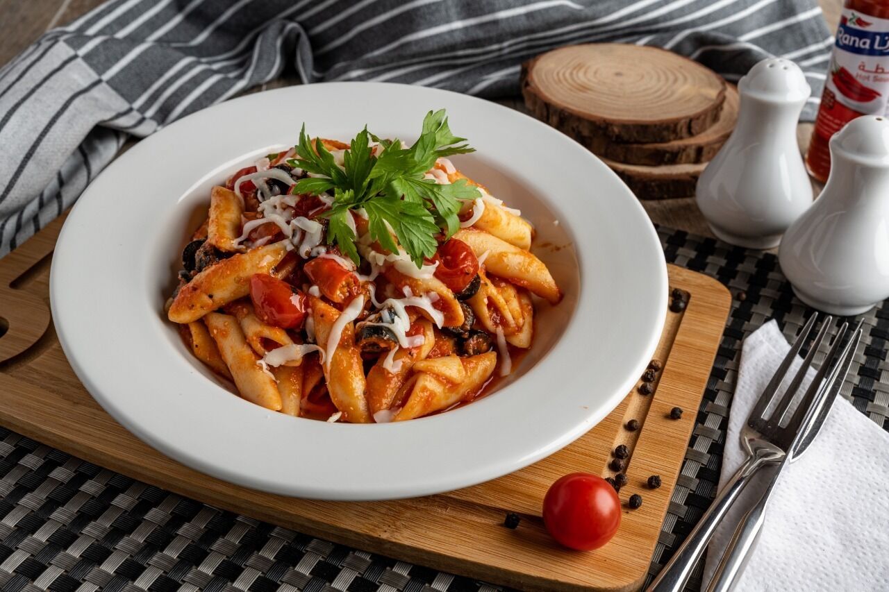 A plate of pasta with a garnish, placed on a wooden board with a striped cloth underneath.