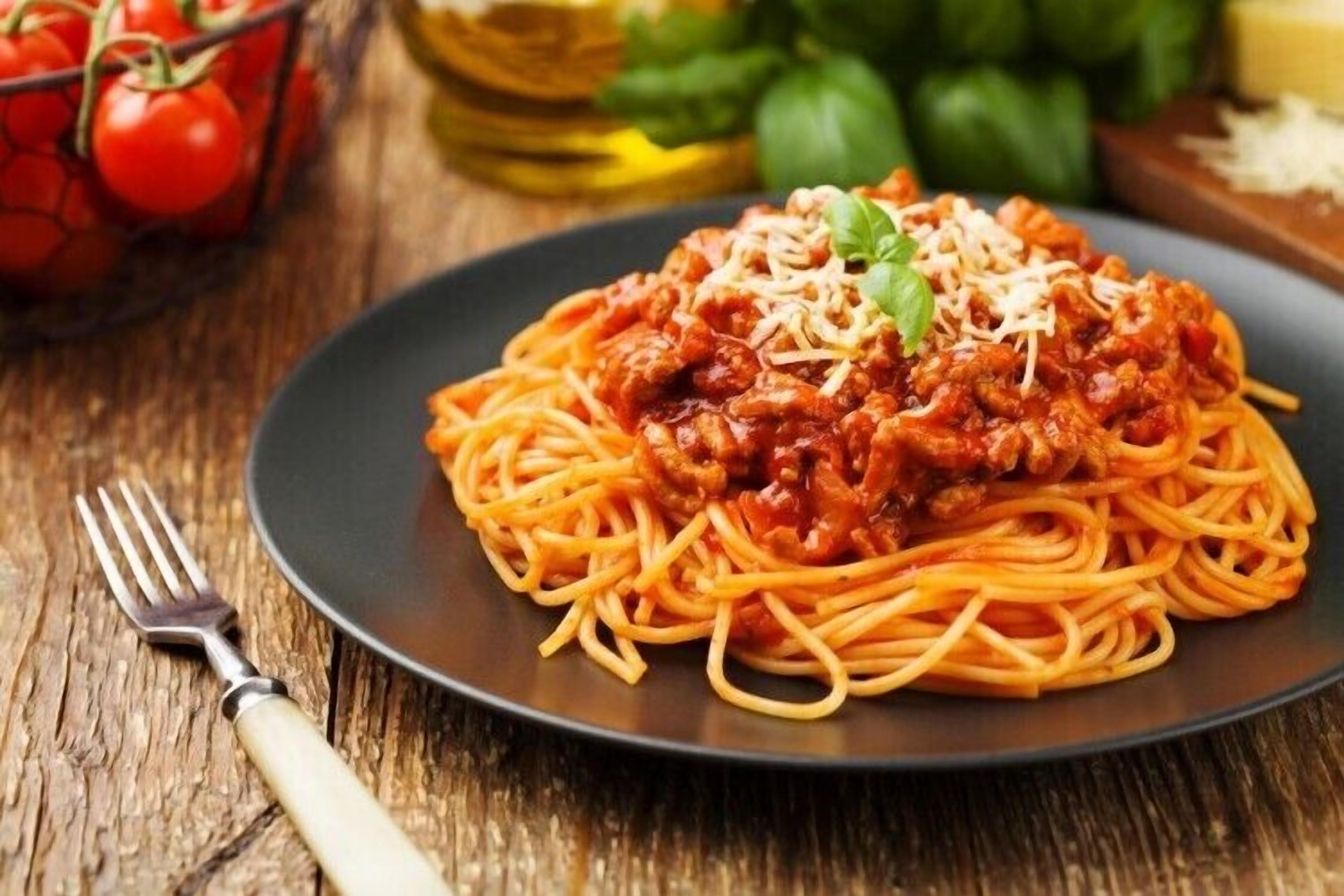 A plate of spaghetti with meat sauce and grated cheese, accompanied by a fork on a wooden table.