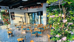 Cafetería interior con mesas y sillas de madera, suelo de terrazo y plantas en macetas.