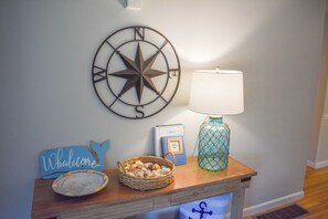 Une table en bois, sur laquelle se trouvent un panier, un tableau encadré, une lampe et une boussole fixée au mur.