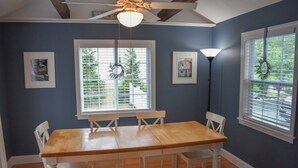 Un comedor con mesa y sillas de madera, ventanas amplias con persianas y un ventilador de techo.