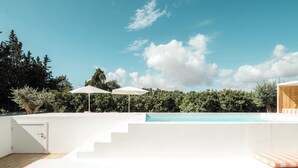 A modern outdoor pool area with a clear blue sky, white walls, and steps leading down to the pool. There are two white umbrellas providing shade. - Casas da Quinta de Cima (Vila Real Santo Antonio)