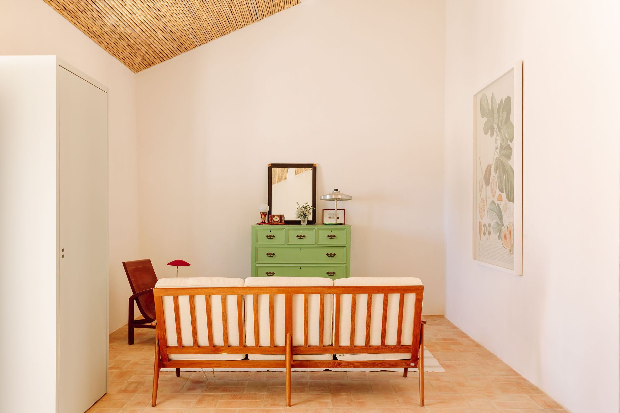 A room with a wooden bench, a green dresser, a mirror, and a framed botanical print on the wall.