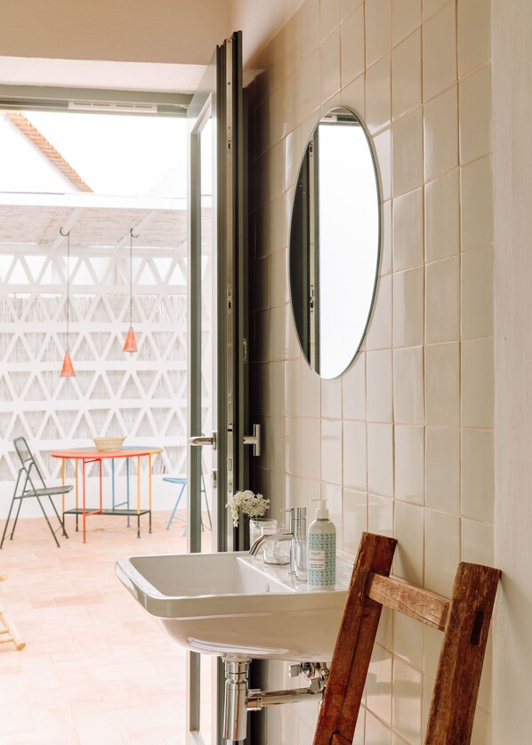 Un baño con un lavamanos blanco, un espejo y un estante de madera.