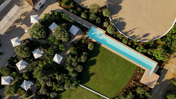 Eine Vogelperspektive zeigt ein Resort mit einem Schwimmbad, Liegebereichen mit Sonnenschirmen und angelegten Gärten.