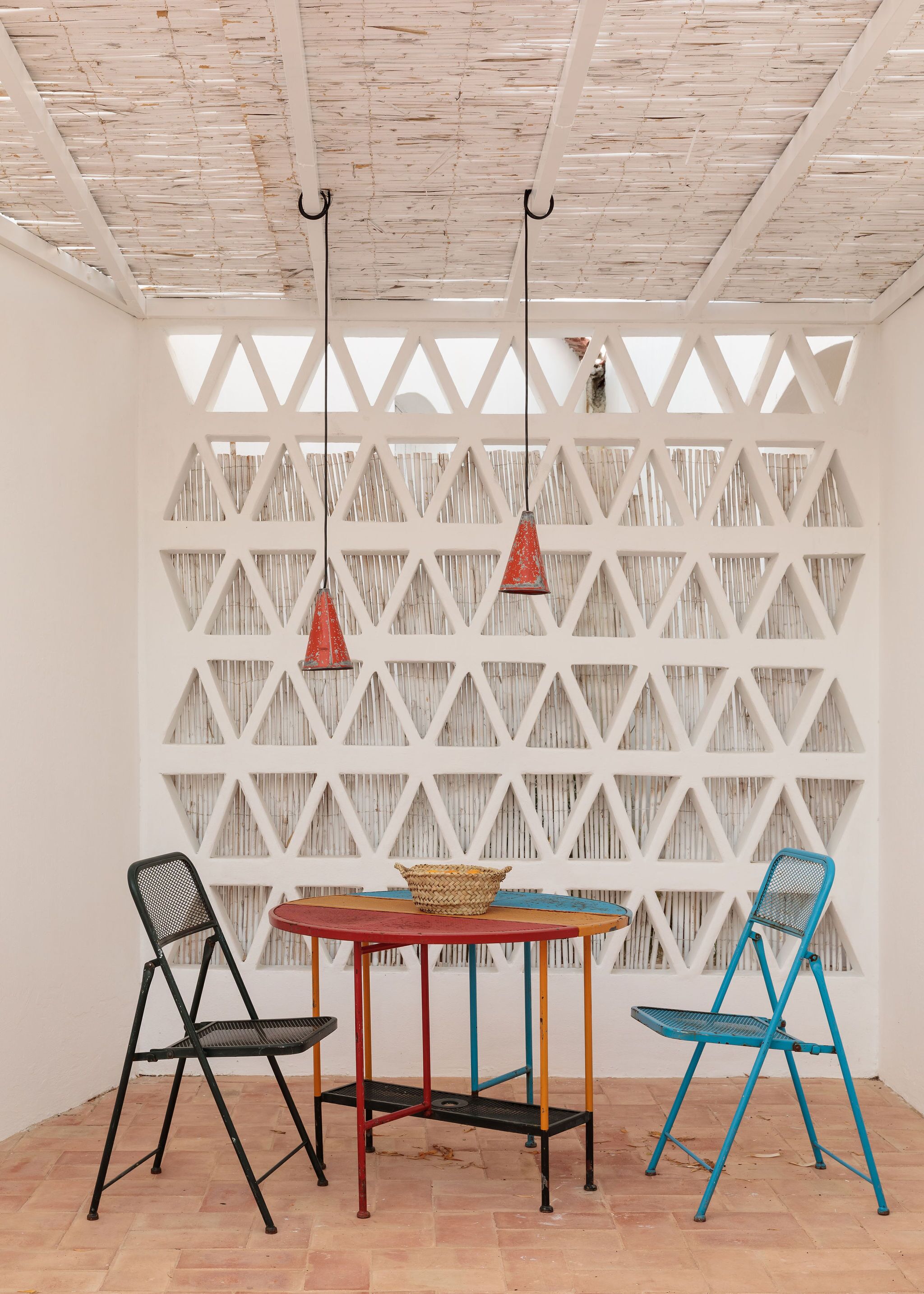 A room with a white lattice wall, a wooden ceiling, a table with chairs, and hanging pendant lights.