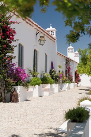 A white building with a tower, a cobblestone path, and flowering plants. - Casas da Quinta de Cima (Vila Real Santo Antonio)