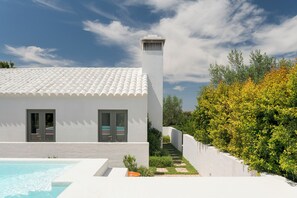 Ein modernes, weißes Gebäude mit einem Ziegeldach, einem Swimmingpool und einer Treppe, die in einen Garten führt.
