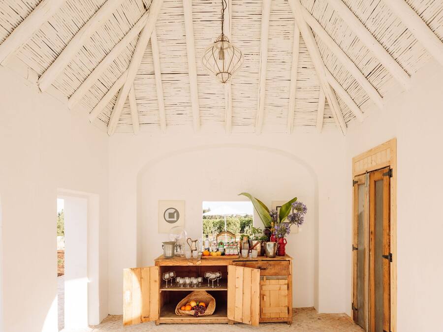 Een rustiek interieur met een houten plafond, een houten kast met glazen servies en een raam met uitzicht op groen.