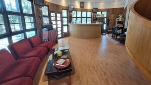A spacious living area with a curved wooden ceiling, a red sofa, a coffee table, and a kitchen area with a bar counter. - Nomads Homestay Sriracha (Si Racha)