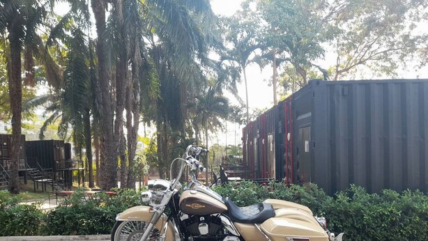 A motorcycle parked in a shaded area with a building in the background. - Nomads Homestay Sriracha (Si Racha)