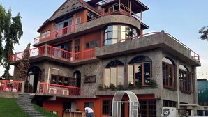 A multi-story building with a curved balcony, a staircase leading to the entrance, and a scooter parked outside. - Nomads Homestay Sriracha (Si Racha)